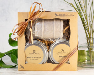 A gift set box containing two soy candles, one with a label reading 'Bathe in Bourbon' and the other with 'Mint Julep' label, and bar soap in a shaped like a bourbon barrel