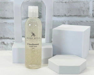 Bottle of Moss Hill Chardonnay handmade bubble bath on a white surface with geometric shapes in the background