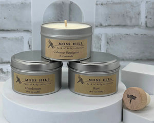 A three piece soy candle set with wine scents. In silver tin containers, stacked on a white surface with a white brick background.