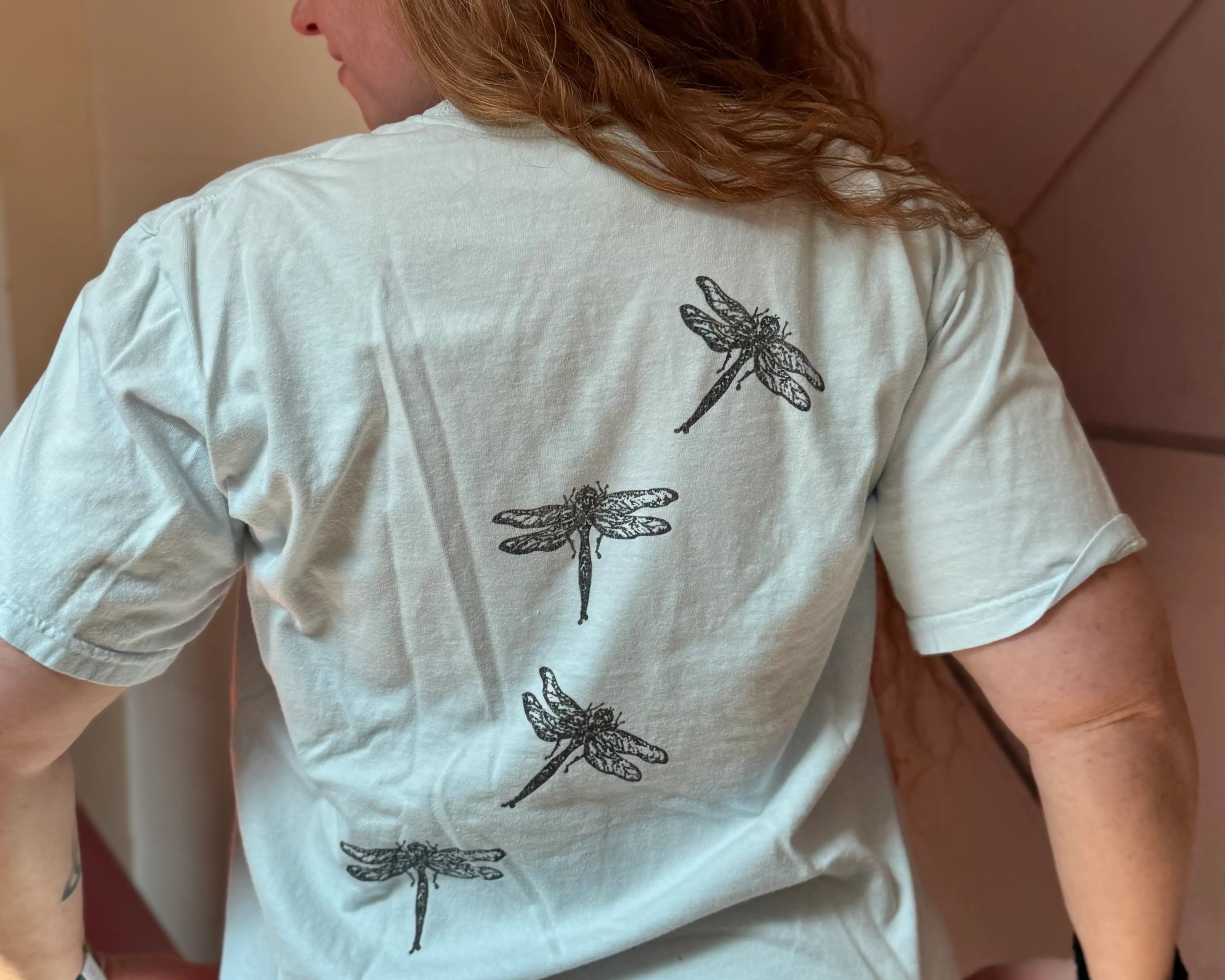 Woman wearing a white Moss Hill Flutter t-shirt with black dragonfly designs on the back.