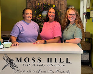 Three women standing behind a counter with 'Moss Hill bath & body collection' branding.