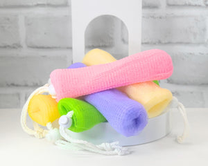 A collection of colorful soap loofas made of mesh, tied with drawstrings, presented in a variety of colors including tan, green, purple, pink, and yellow.
