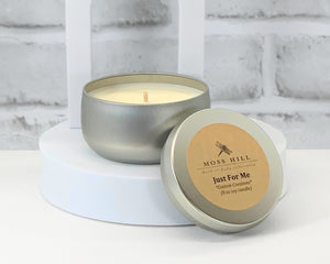 An 8 oz metal container candle with lid on a white surface with a branded label that reads 'Just For Me' for custom candles.