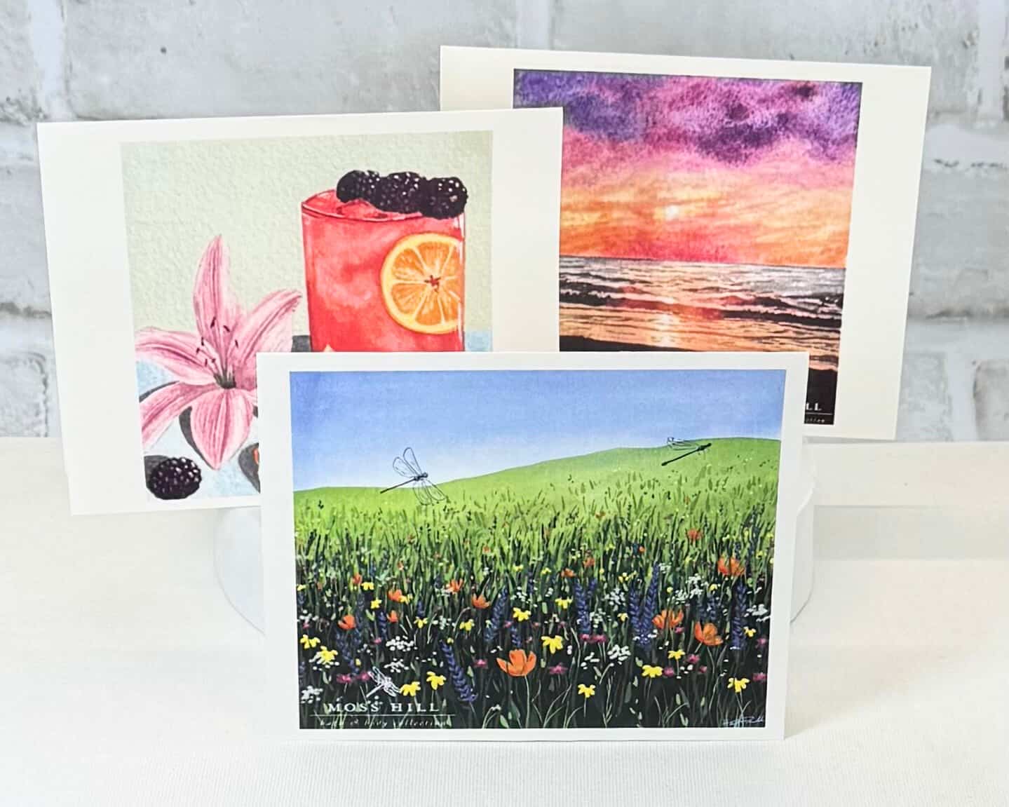 Set of four greeting cards with watercolor designs on a white surface. Showcasing Moss Hill scent profiles