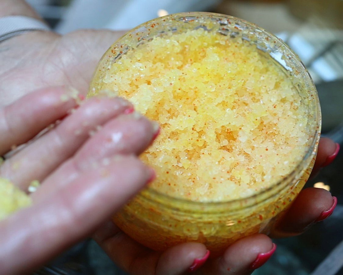 Clear container with yellow sea salt body scrub in it and being shown on someones hand.