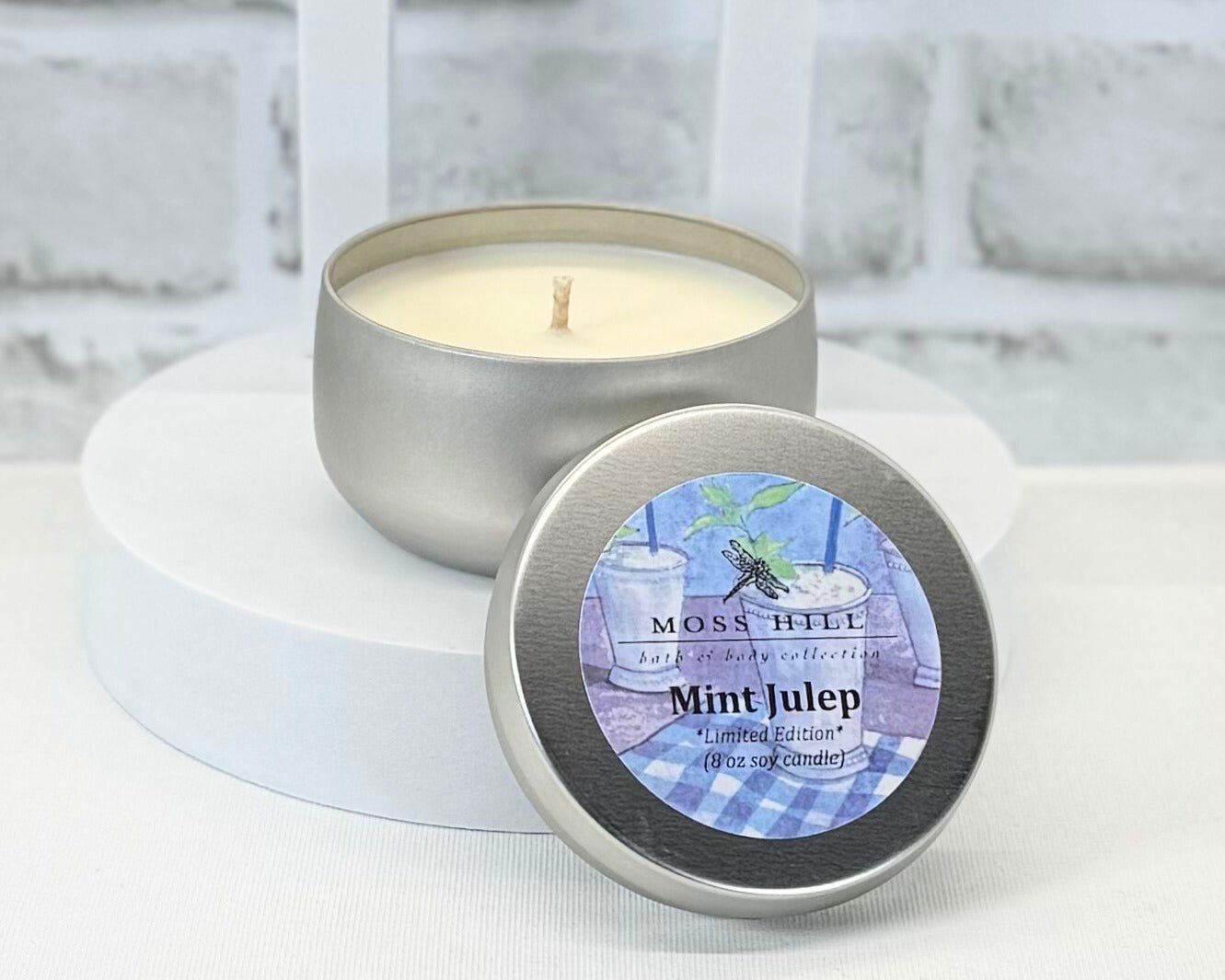 An 8 oz soy candle in the scent Mist Julep. In silver colored tins, with a label of the Moss Hill Bath & Body Logo.