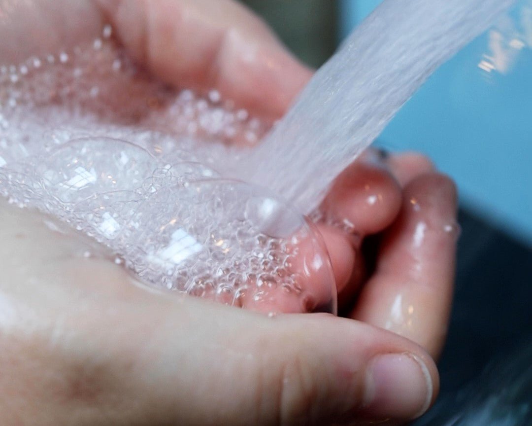 Running water creating soap suds in cupped hands.