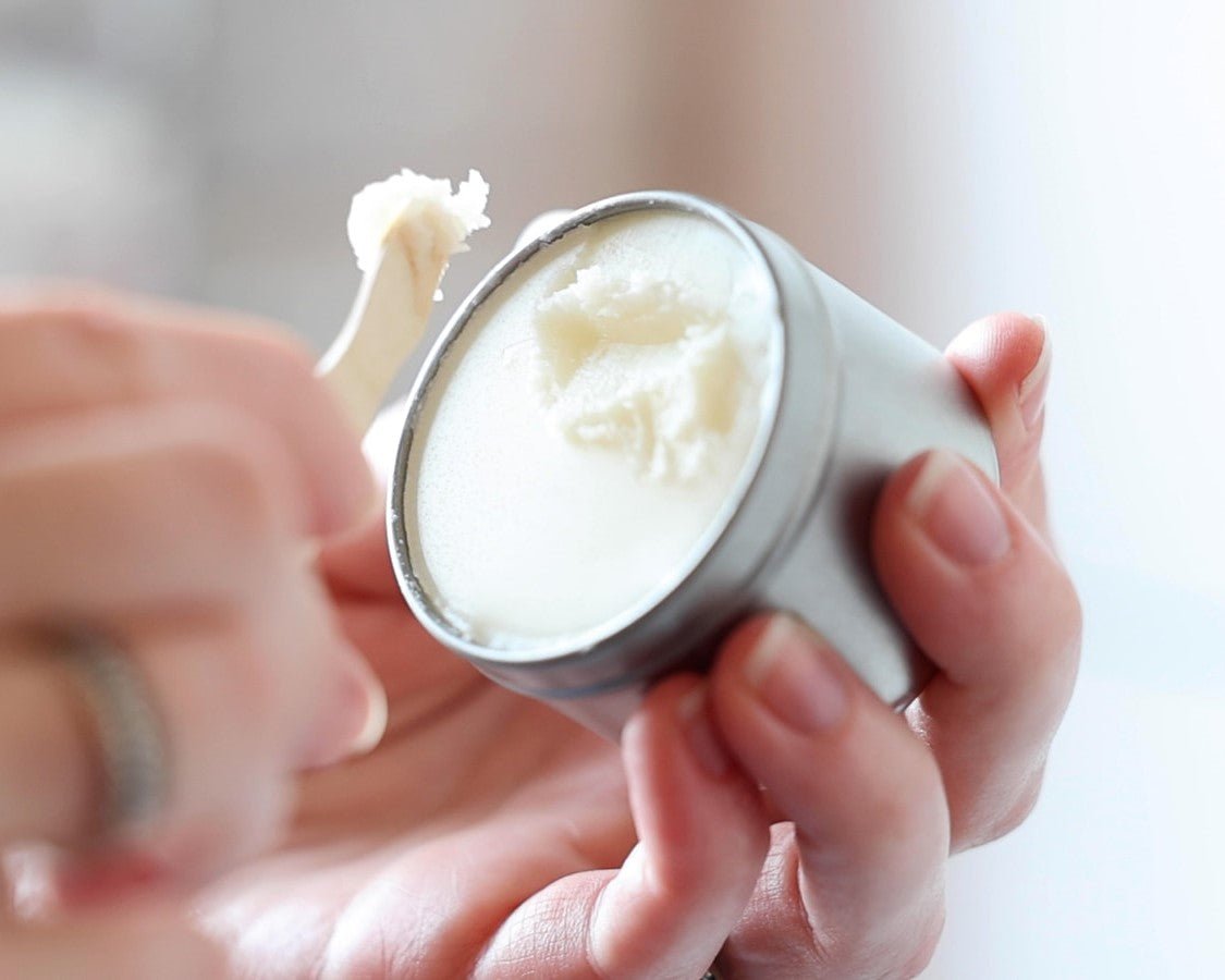 Hand holding a container of white Dry Skin Relief Balm with a blurred background