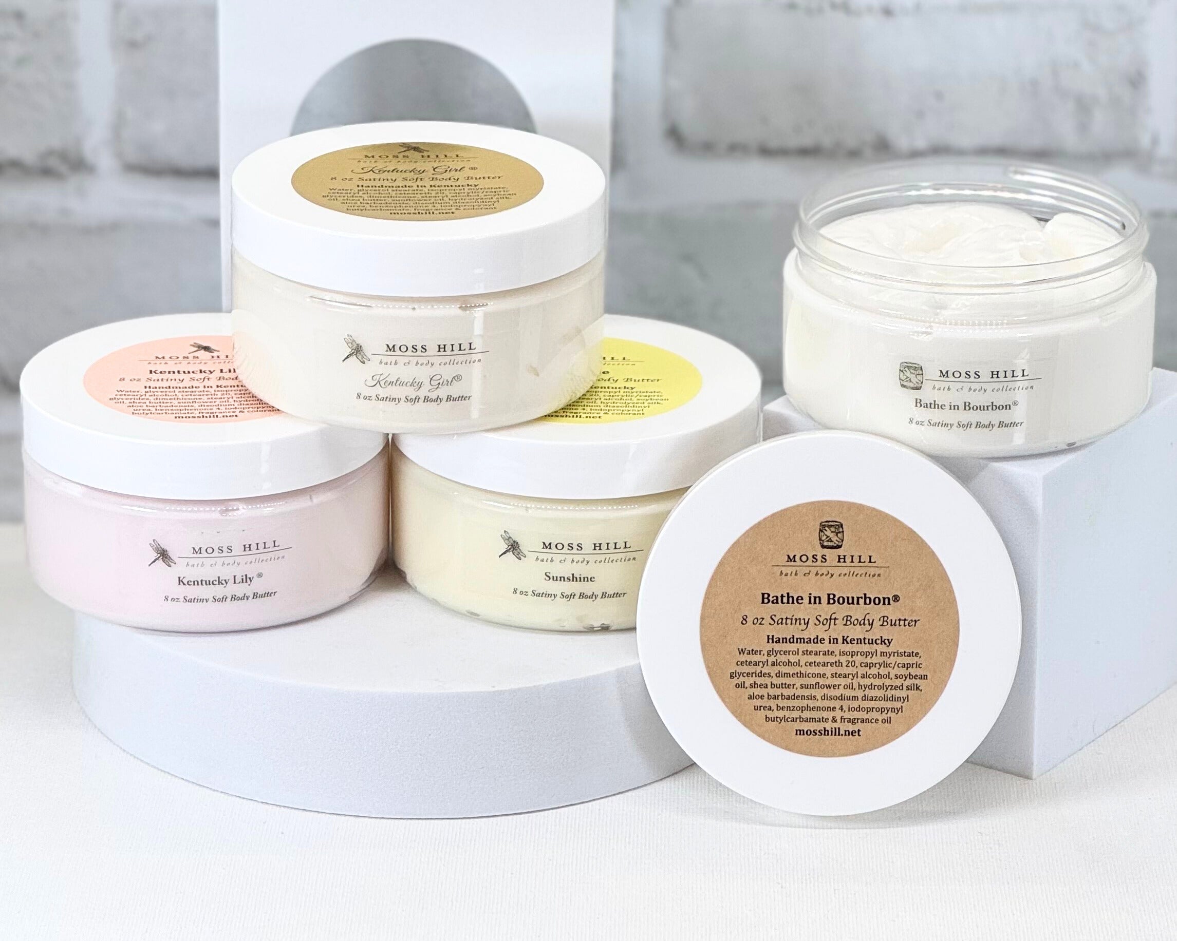 Jars of handmade body butter with different labels, arranged in a stacked fashion with one jar open showing the product inside.