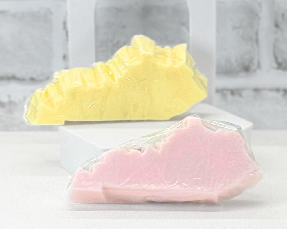 Two bar soaps shaped as the state on Kentucky in yellow and pink.