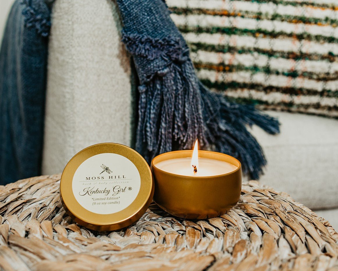 A 8 oz soy candle hand poured into a gold tin with the lid removed from the candle and a wick with a flame at the end burning