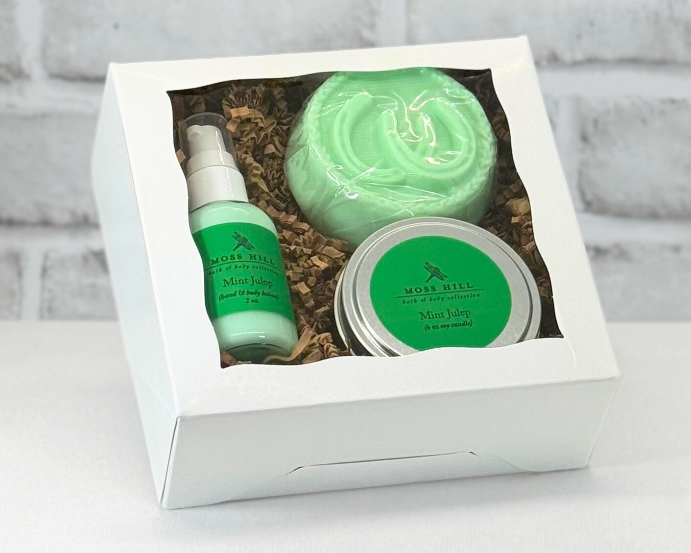 3 piece body care gift box set with bar soap, hand a body lotion, and a 6 oz soy candle in the scent Mint Julep. Wrapped in a white box with brown filler paper.