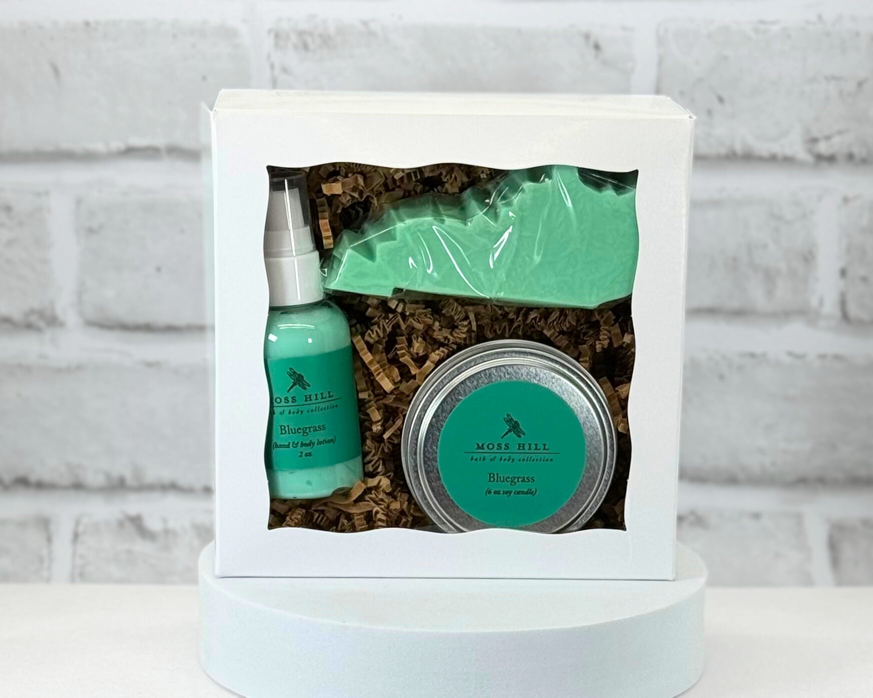 A gift set containing a candle, lotion, and a Kentucky shaped soap packaged in a white box with a clear viewing window. In the scent Bluegrass.