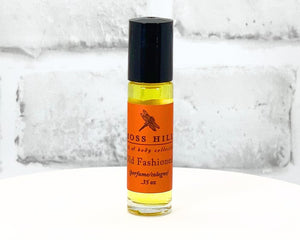 Old Fashioned travel-sized roll-on perfume bottle with orange label displayed on a white stand.