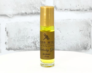 Kentucky Girl travel-sized roll-on perfume bottle with yellow label displayed on a white stand.