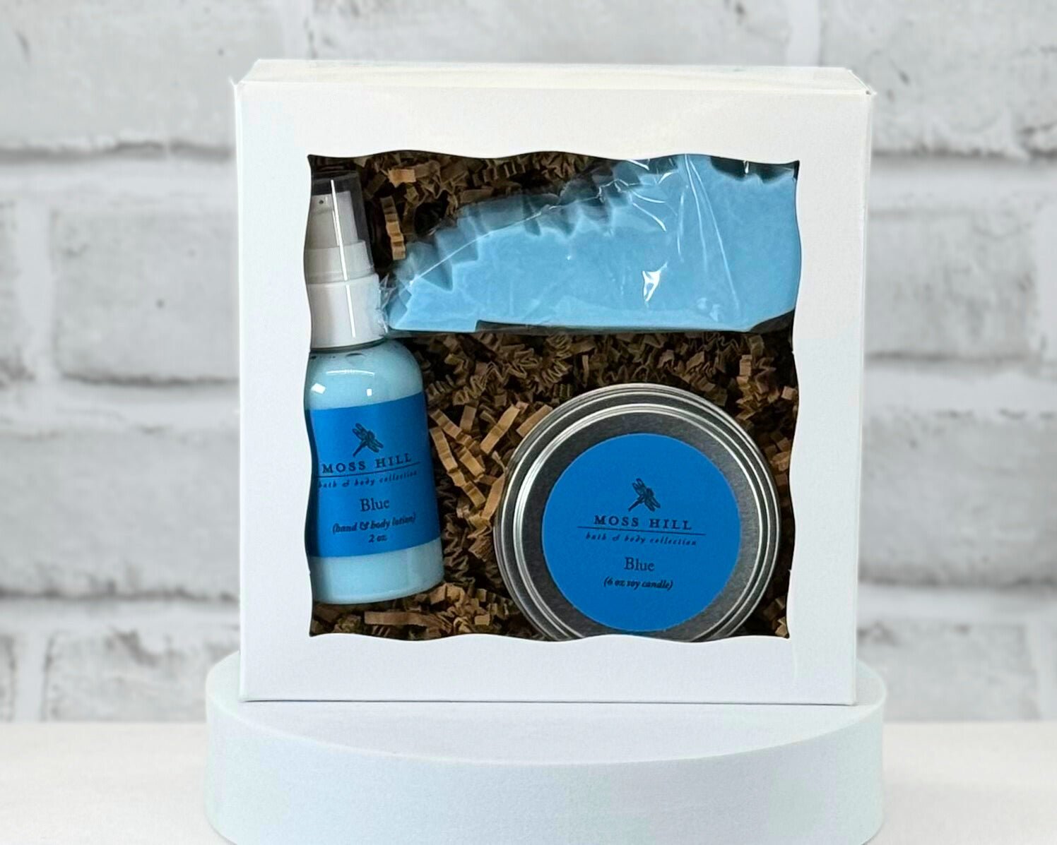 A gift set containing a candle, lotion, and a Kentucky shaped soap packaged in a white box with a clear viewing window.