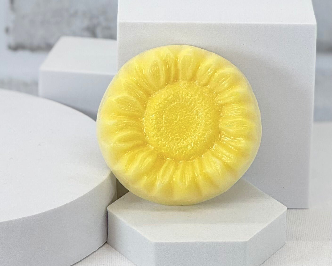 A handmade soap bar with a pattern of a sunflower, placed on a white surface.