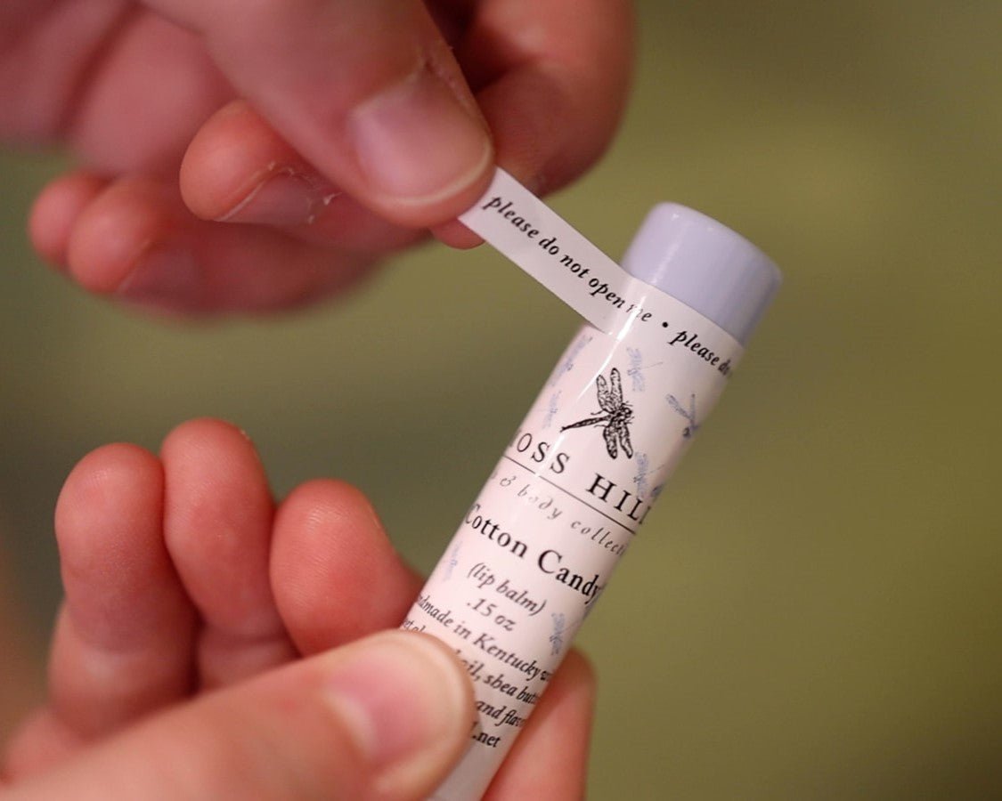 Cotton Candy labeled lip balm being held why a 'do not open me' sticker is being applied to the lid.