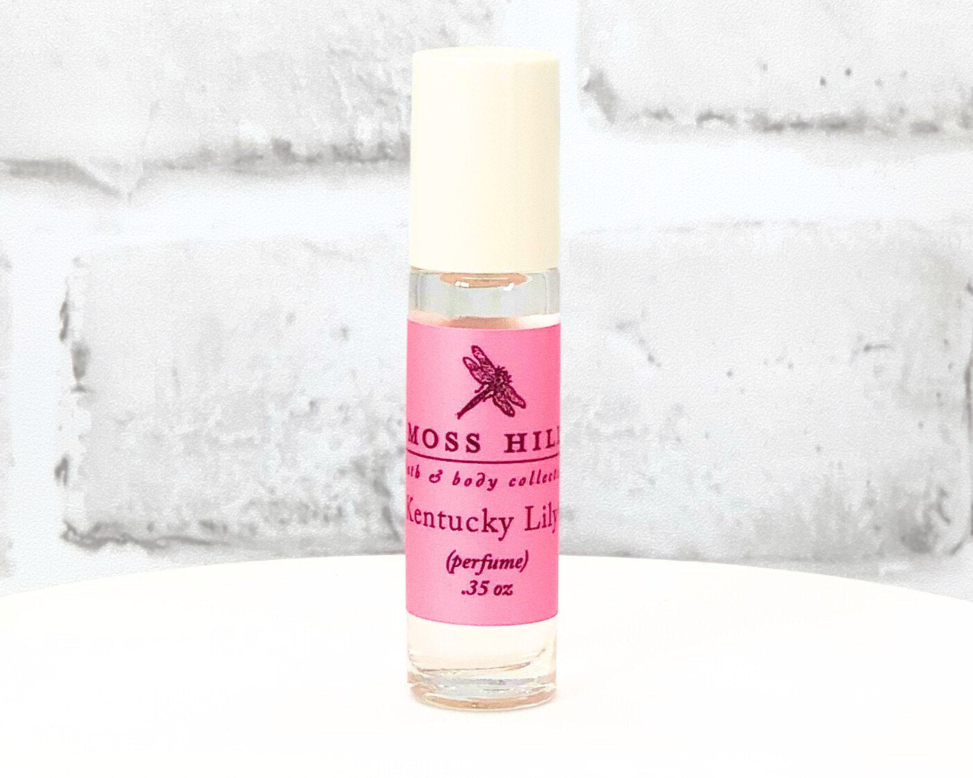 Kentucky Lily travel-sized roll-on perfume bottle with pink label displayed on a white stand.