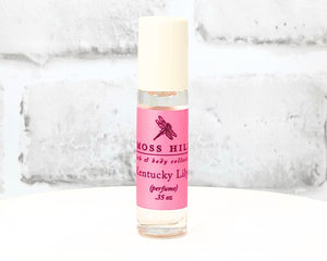 Kentucky Lily travel-sized roll-on perfume bottle with pink label displayed on a white stand.