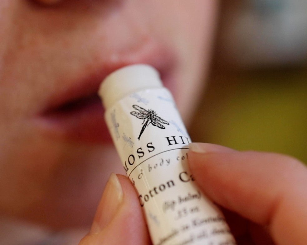 Lip balm wrapped in the moss hill dragonfly logo being applied to lips.