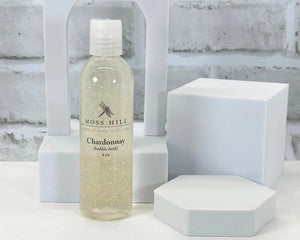 Bottle of Moss Hill Chardonnay handmade bubble bath on a white surface with geometric shapes in the background