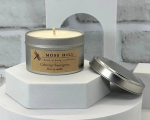 A soy candle in the scent cabernet sauvignon. Hand poured into a silver tin. Sitting on a white surface.