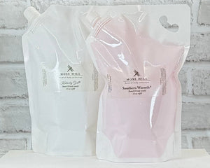 Two refill pouches of Moss Hill Hand & Body Wash, one labeled 'Southern Warmth' in pink, and the other Kentucky Girl in white.