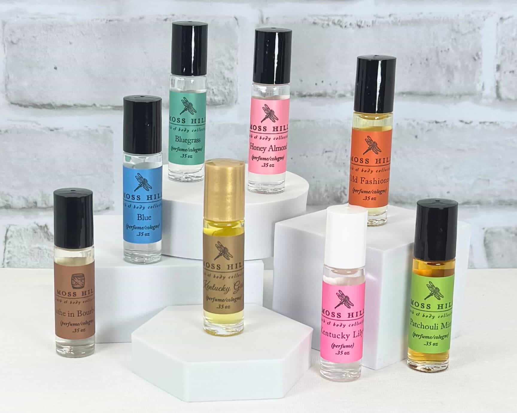 Collection of Moss Hill Roll-On Perfume bottles on a white surface with a light gray brick wall background.