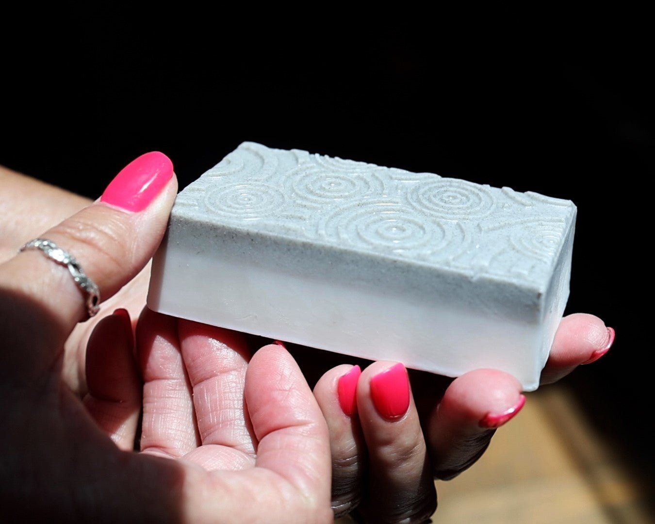 A woman hands holding a bar of exfoliating bar soap with embossed details.