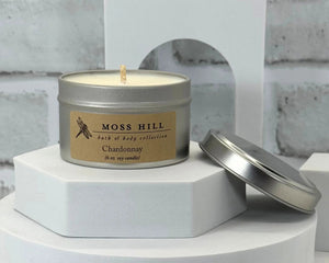 A Chardonnay scented soy candle hand-poured into a silver tin. Sitting on a white stand with a white background.