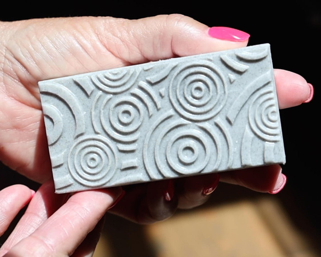 A woman holding an embossed detailed bar soap that intended to be an exfoliating soap scrub for your hands and body.