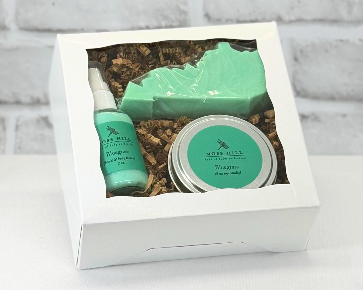 A self care gift set containing a candle, lotion, and a Kentucky shaped soap packaged in a white box with a clear viewing window. In the scent Bluegrass.