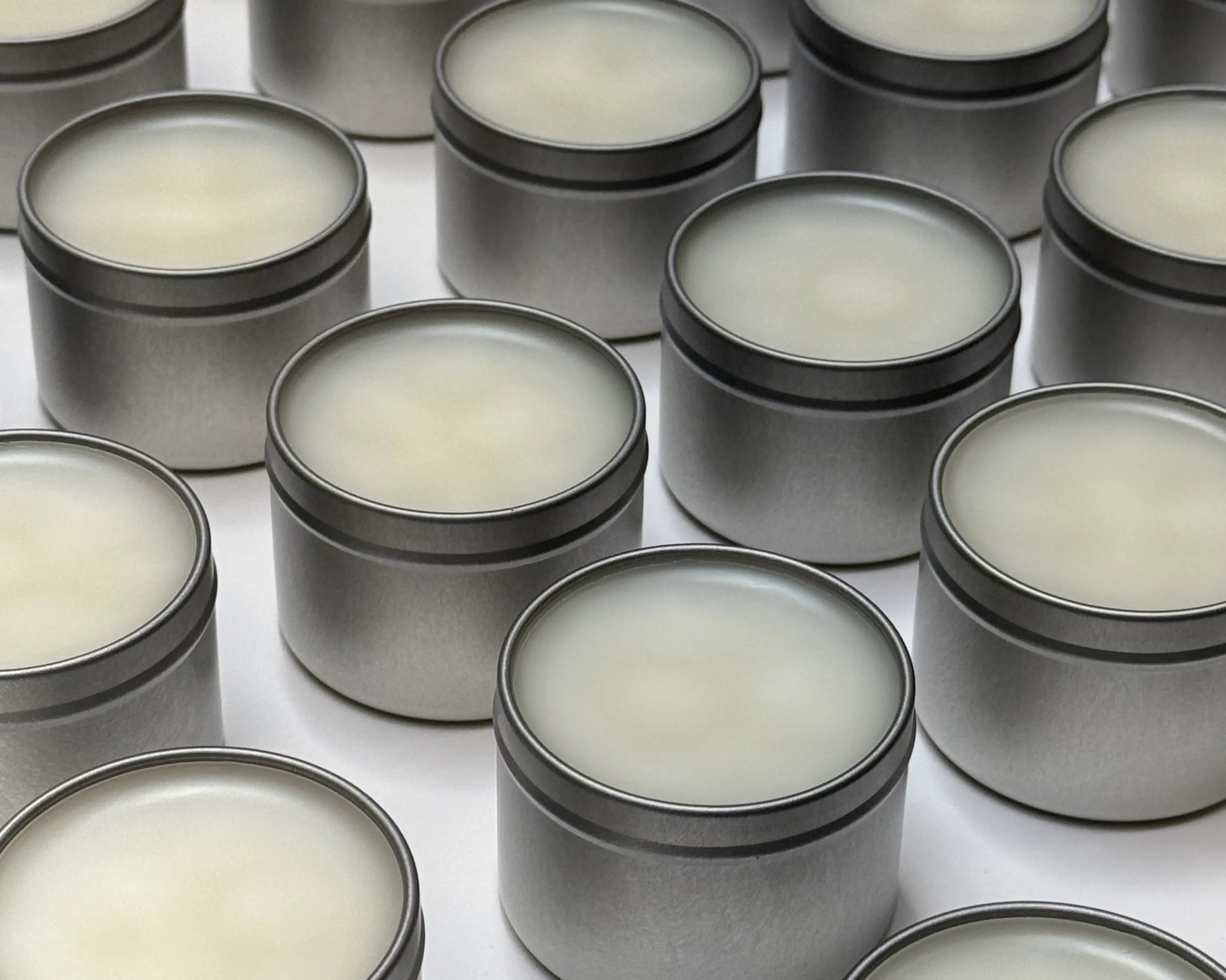 Image of hand-poured soy candles in a silver tin sitting on a white table top.