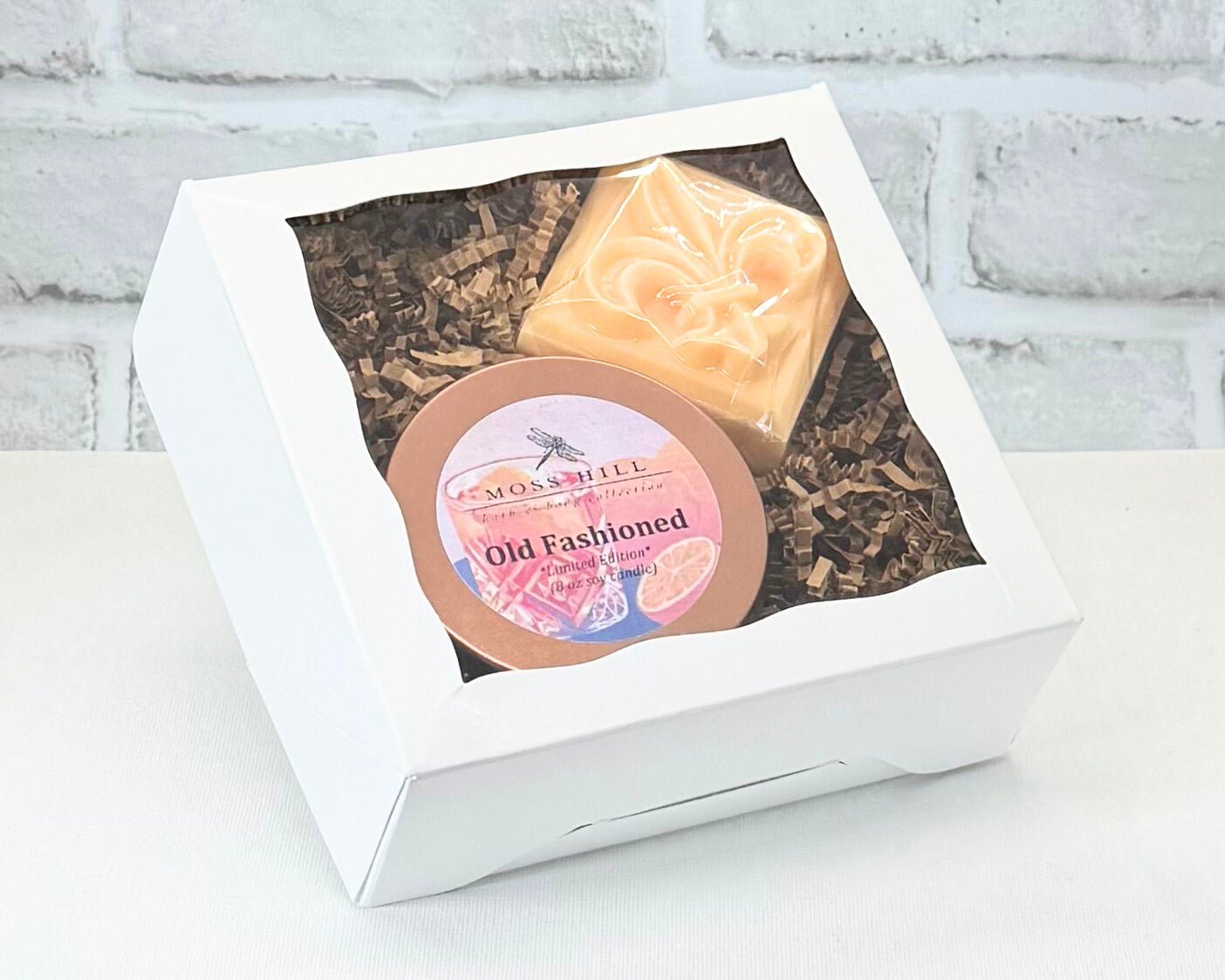 Two piece gift box set in the scent Old Fashioned. It comes with a handmade soap with a fleur-de-lis on top and an 8 oz soy candle. Beautifully styled in a white box by Moss Hill Bath & Body.
