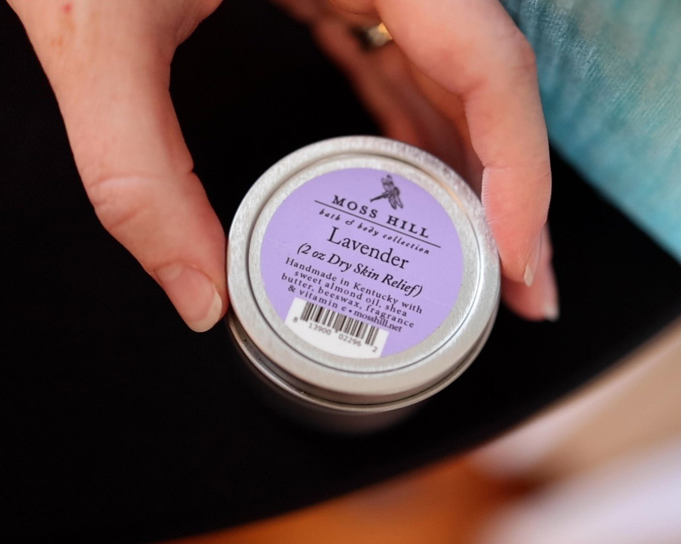 Two fingers holding a silver tin of dry skin relief. Handmade in Kentucky with almond oil, shea butter, beeswax, fragrance & vitamin C