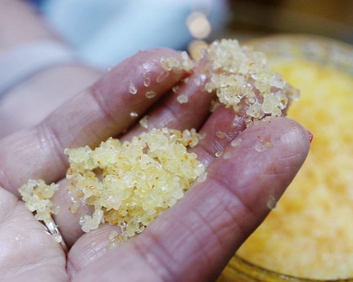 Yellow body scrub on fingers with close up detail of the body care product.
