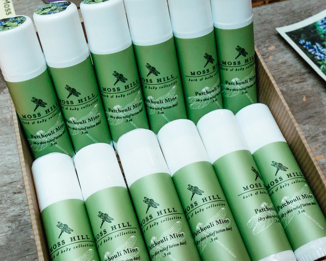 Several white tubes wrapped in green labels of dry skin relief lotion bar sitting in a decorative box on a product display table.