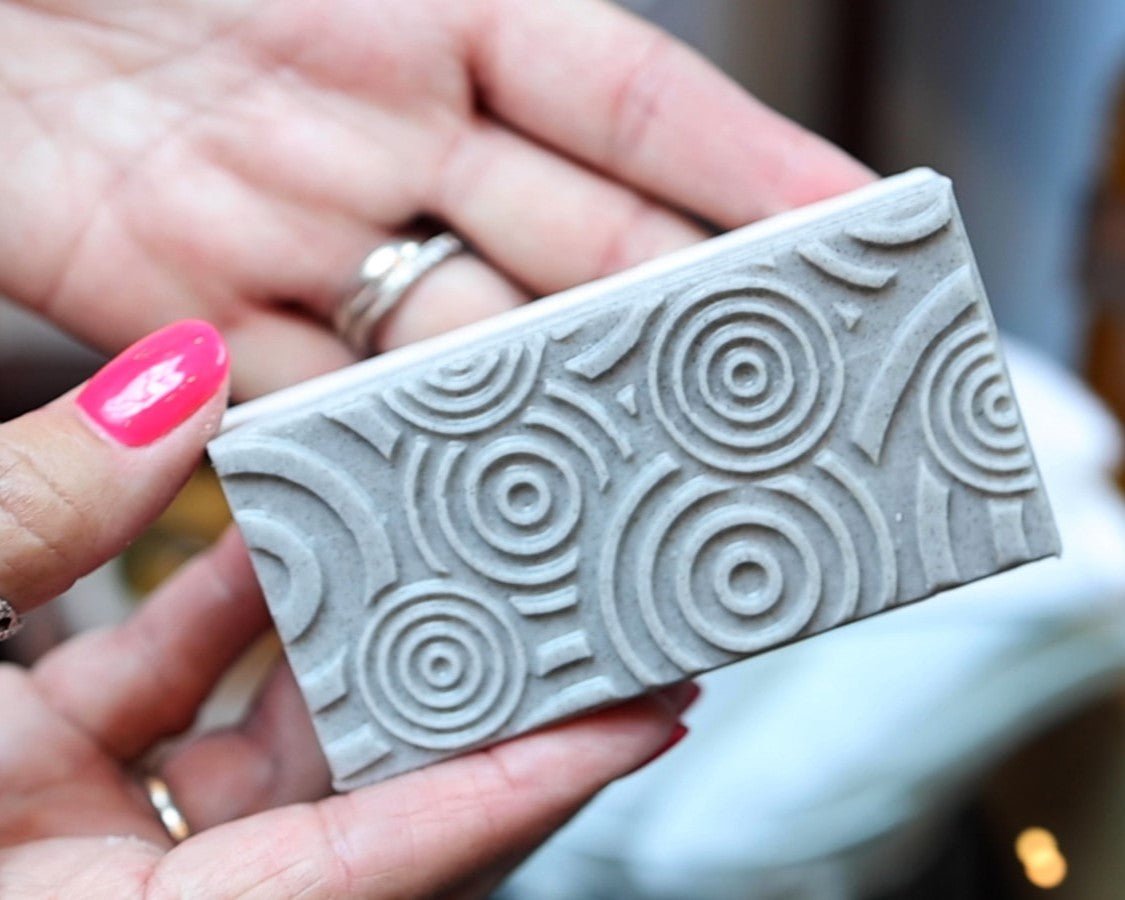Exfoliating bar soap with embossed details on the top being held by two hands.