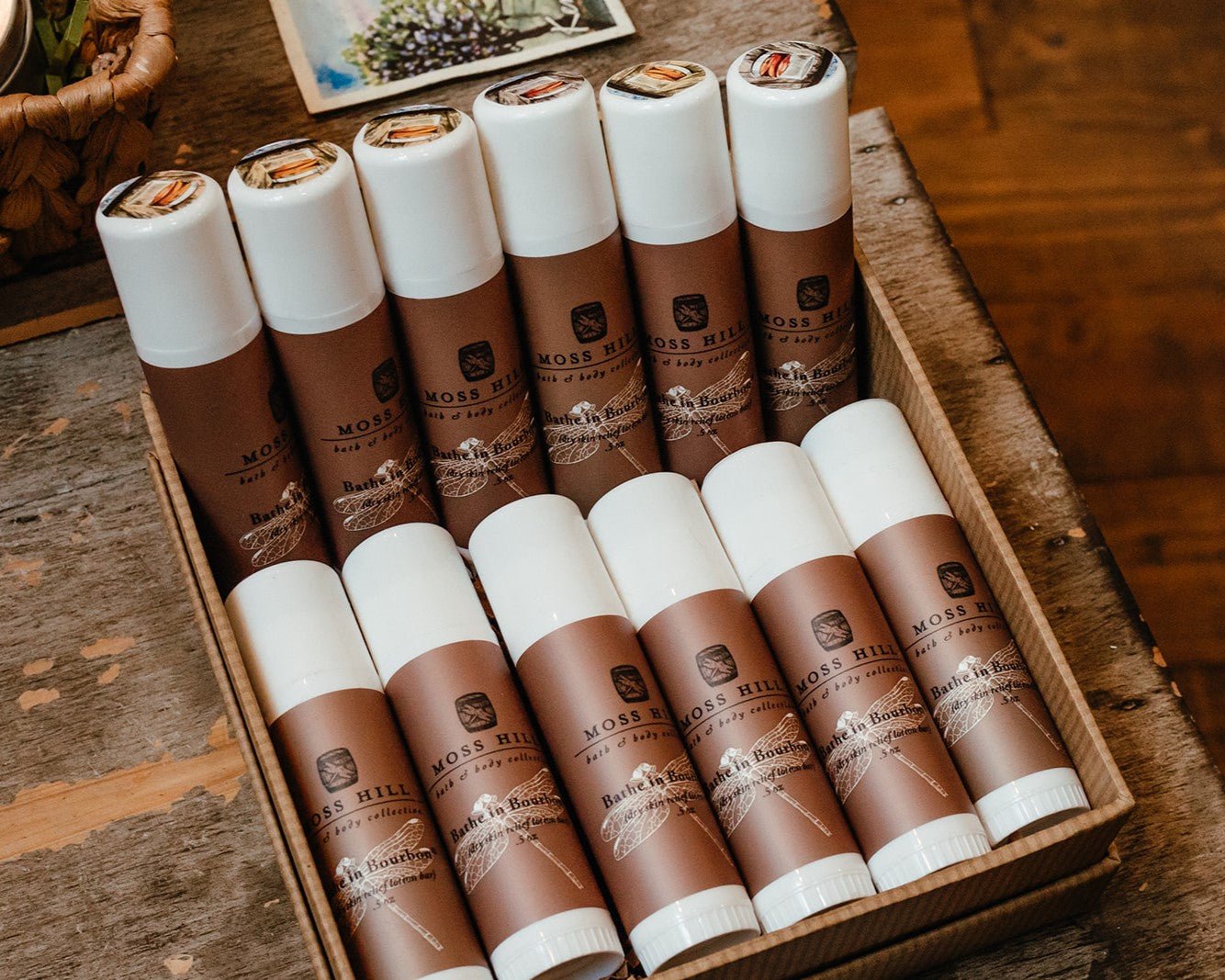 White tubes of Dry Relief Lotion Bar wrapped with a brown label with several laying in a box on a table display.