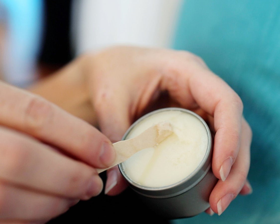  hand holding a wooden spoon scooping out dry skin relief from a 2 oz silver tin.