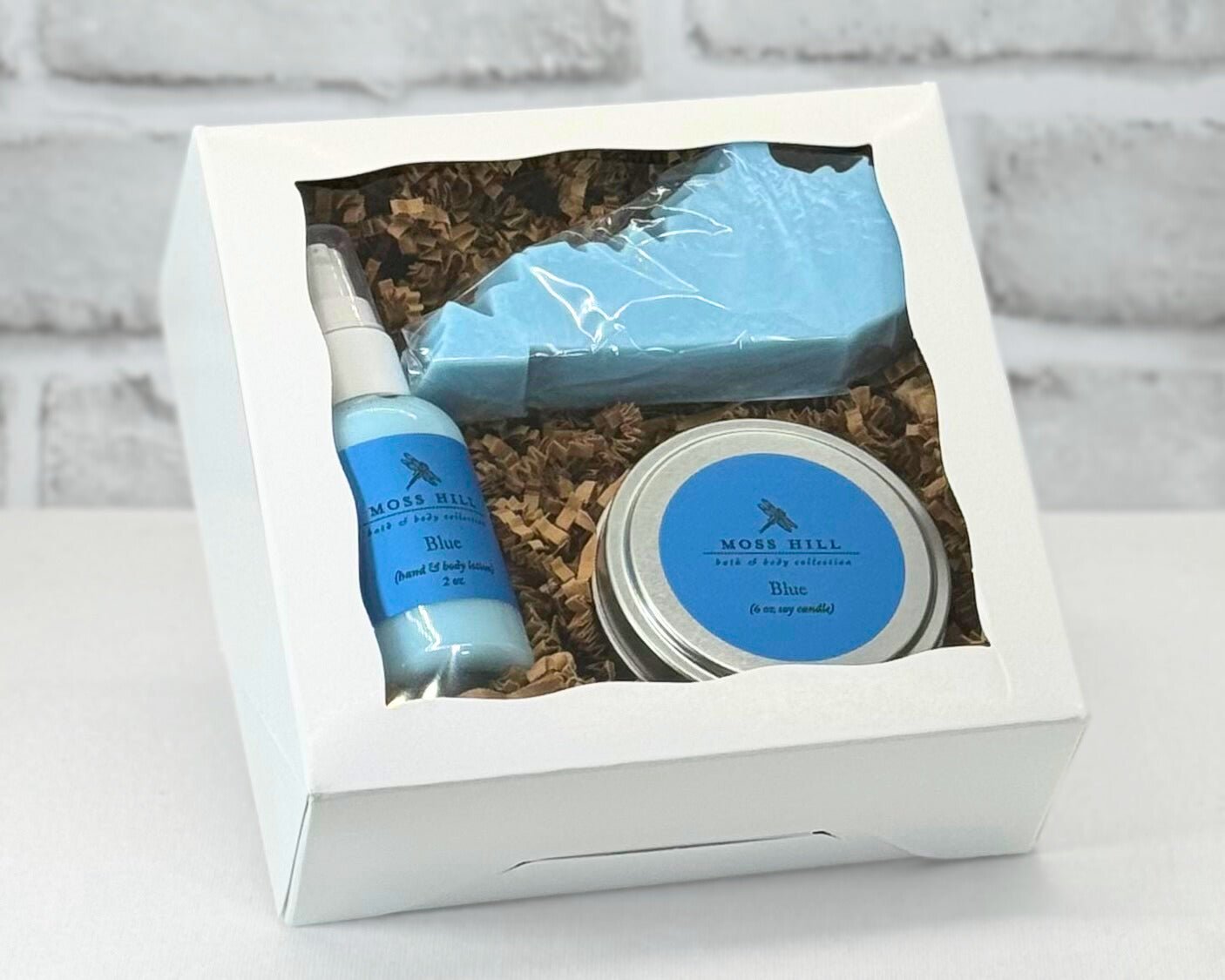 A gift set containing a candle, lotion, and a Kentucky shaped soap packaged in a white box with a clear viewing window. In the scent Blue.