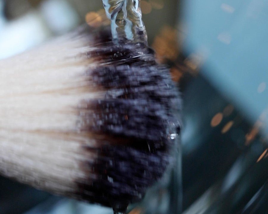 Shaving cream on a shaving brushed being rinsed off with water.