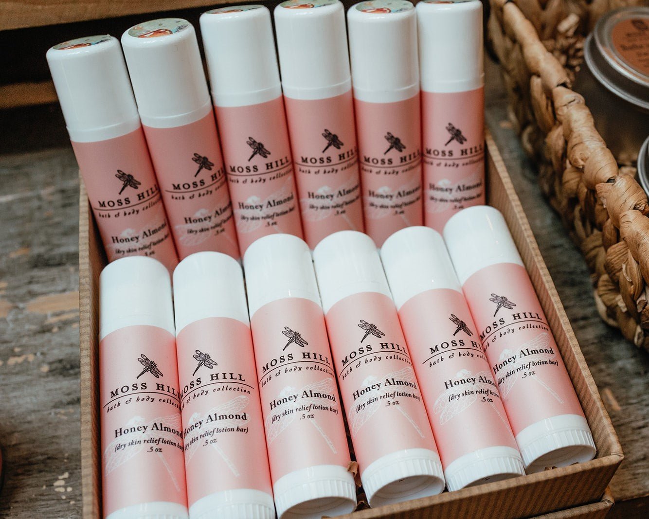 White tubes wrapped with a pink label that says Moss Hill Dry Skin Relief Lotion Bar sitting in a box on top of a table display.