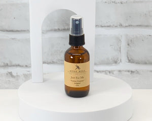 A brown spray bottle of Cologne labeled ' Moss Hill Custom Creations ' on a white surface with a brick wall in the background.